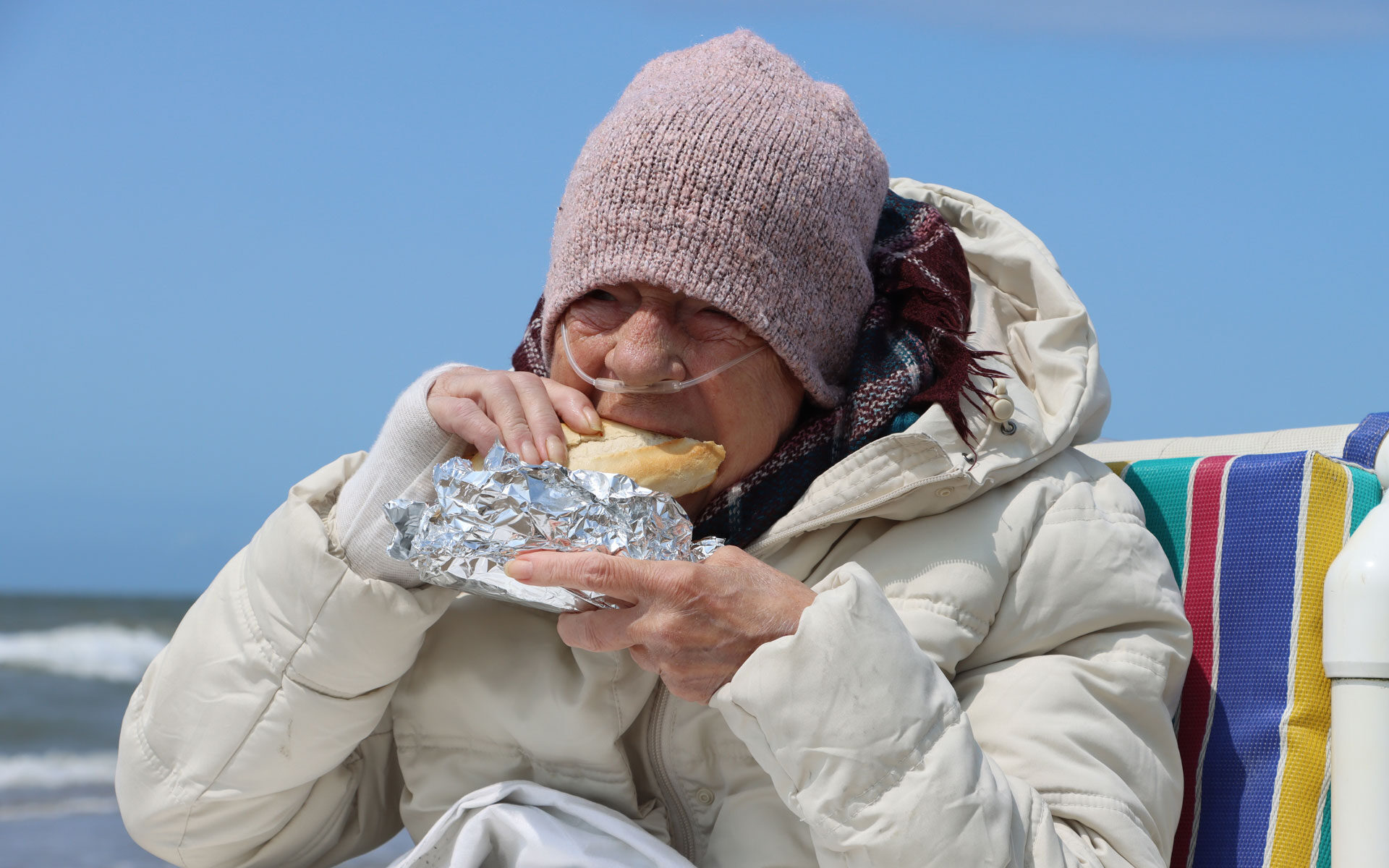 Kranke Frau im Rollstuhl am Meer isst ein Fischbrötchen