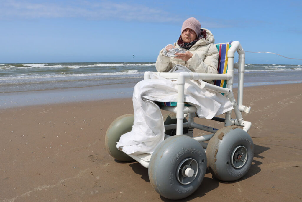 Kranke Frau mit einem Strandrollstuhl am Meer