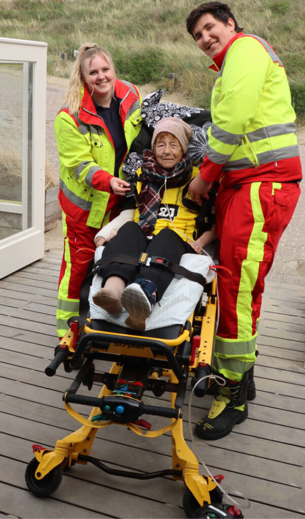 Zwei Rettungssanitäter setzen eine kranke Frau in einen Transportstuhl