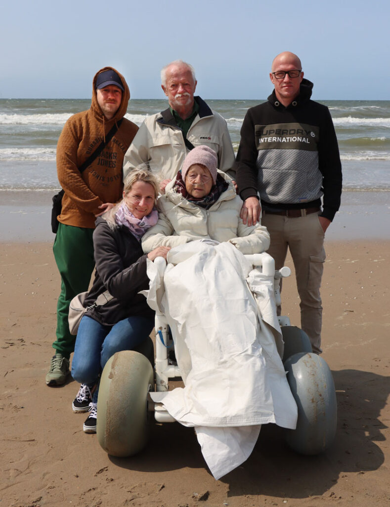 Kranke Frau im Rollstuhl mit ihrer Familie am Meer